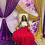 child, girl, dress, red_dress, white_top, glasses, chair, throne, purple_curtains, gold_curtains, carpet, indoor, smiling, portrait, formal_wear, decorations, event, flooring, long_hair, fashion