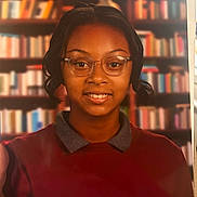 Zhyonnia joined the competition — help win amazing prizes! person, child, glasses, smile, portrait, indoors, sweater, collar, bookshelf, background, young, face, head, short_hair, brown_skin, casual_clothing, eyewear, happy, education, library