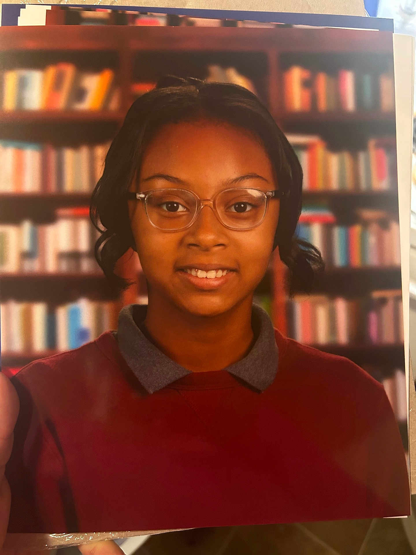 Zhyonnia joined the competition — help win amazing prizes! person, child, glasses, smile, portrait, indoors, sweater, collar, bookshelf, background, young, face, head, short_hair, brown_skin, casual_clothing, eyewear, happy, education, library