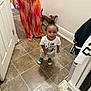 Carmelo joined the competition — help win amazing prizes! toddler, child, person, indoor, floor, tile, dog, pet, adult, pants, green_shoes, white_shirt, hair_bun, smiling, standing, wall, door, home, casual, curious