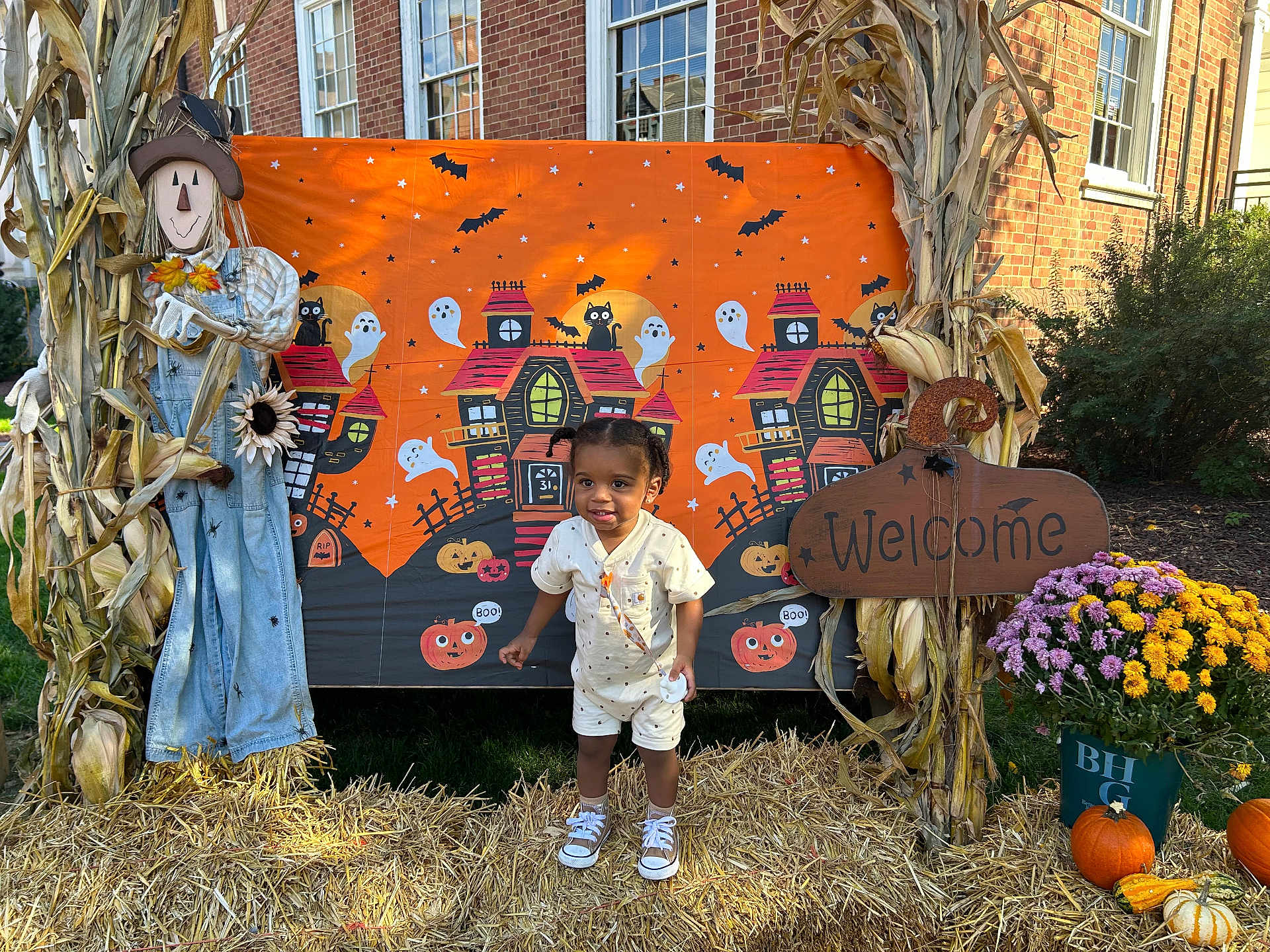 Carmelo is registered to the contest to win money with this photo: toddler, child, halloween, pumpkin, scarecrow, cornstalks, welcome_sign, flowers, hay, haunted_house, ghost, bat, brick_building, outdoor, costume, smiling, grass, daylight, festive, portrait