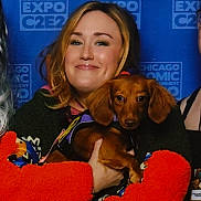 Daisy Mae is registered to the contest to win money with this photo: person, dog, dachshund, pet, smile, hair, face, clothing, hand, background, expo, event, indoor, portrait, cute, animal, brown, holding, happy, furry