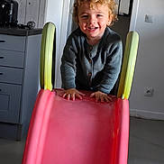 Kaylio Vinot participe au concours pour gagner de l'argent avec cette photo : cabinet, child, climbing, curly_hair, doorway, floor, grey_sweater, happy, home, indoor, kitchen, light_switch, person, pink_slide, play, slide, smiling, toddler, toy, young_child