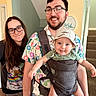 Dominic joined the competition — help win amazing prizes! baby, man, woman, glasses, baby_carrier, indoor, smile, tongue_out, staircase, casual_clothing, family, portrait, happy, home, person, shorts, hat, long_hair, beard, tshirt