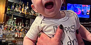 Theo joined the competition — help win amazing prizes! baby, bar, bottle, clothing, counter, drink, face, glass, hand, happy, holding, indoor, infant, light, onesie, person, portrait, smiling, tattoo, watch