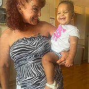 Zamyah is registered to the contest to win money with this photo: adult, baby, clothing, dress, eveningdress, face, female, formalwear, happy, hardwood, head, indoors, laughing, person, photography, portrait, skin, tattoo, woman, wood