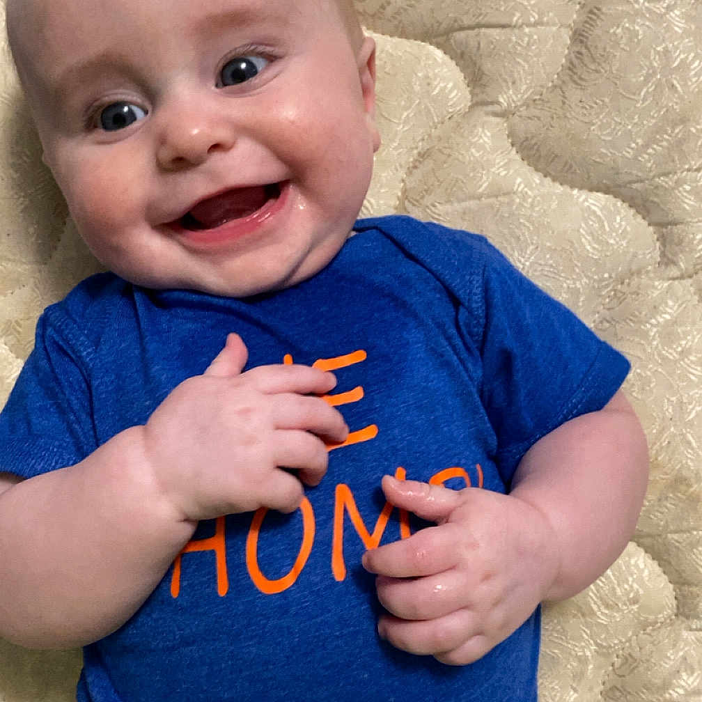 Troy is registered to the contest to win money with this photo: applique, baby, bodypart, clothing, face, finger, hand, happy, head, laughing, mouth, pattern, person, photography, portrait, shorts, sitting, smile, t_shirt, teeth