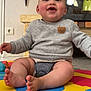 baby, child, smiling, indoor, play_mat, sweater, teddy_bear_patch, toes, happy, floor, couch, fireplace, toy, cute, infant, person, head, face, legs, seated