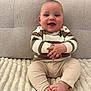 baby, child, smiling, sitting, striped_sweater, beige_pants, soft_blanket, couch, indoors, portrait, happy, cute, infant, hands, feet, cozy, warm_clothing, closeup, face, person