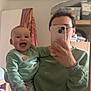 Thélyo participe au concours pour gagner de l'argent avec cette photo : baby, adult, mirror, selfie, smiling, indoor, sweater, glasses, phone, furniture, cabinet, blanket, wooden_floor, person, holding, happy, face, casual_clothing, home, portrait