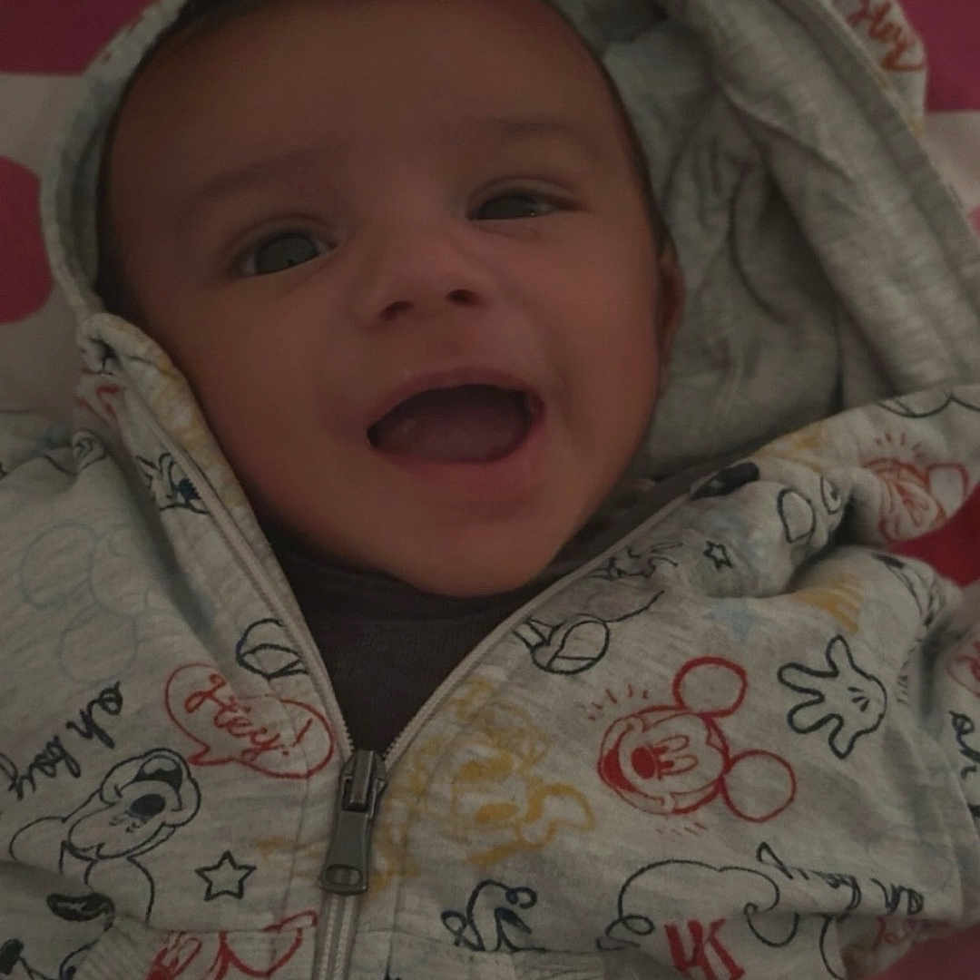 Yanis a rejoint le concours — aidez-le/la à gagner de superbes lots ! apparel, baby, bed, blanket, cartoon_print, child, clothing, cozy, cute, fabric, face, happy, hoodie, indoor, infant, person, portrait, smile, young_child, zipper