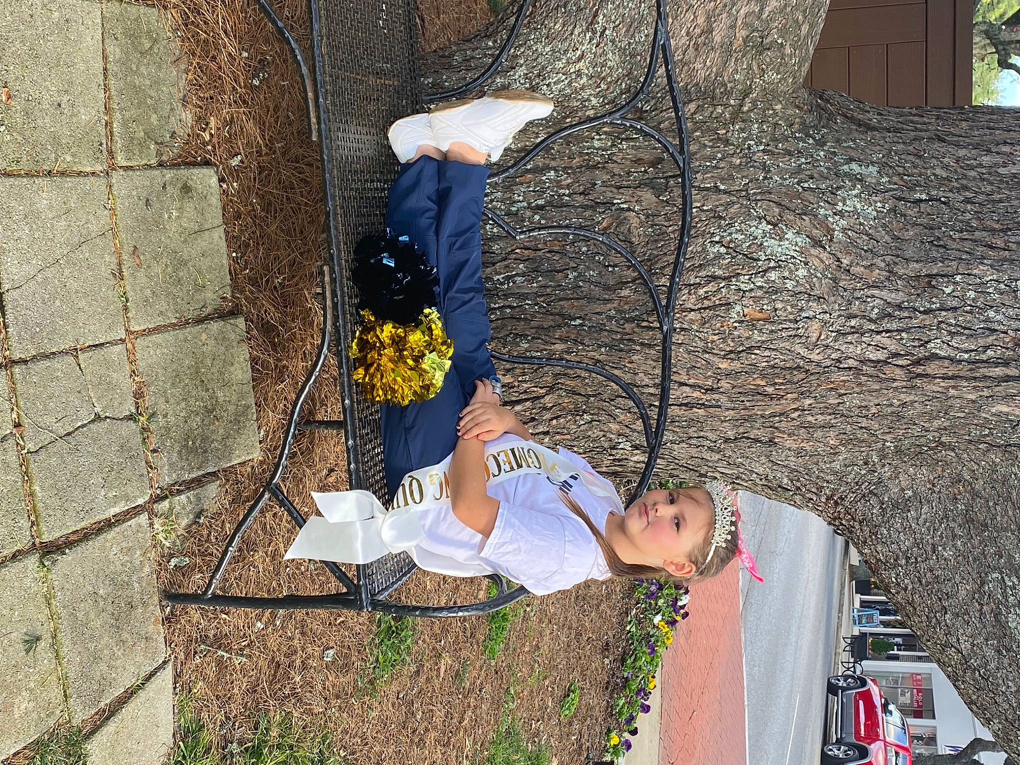 Reagan is registered to the contest to win money with this photo: car, facade, flower, fun, headwear, leisure, person, plant, recreation, road_surface, shadow, sidewalk, sitting, street, tree, visual_arts, wall, wood