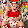 baby, blanket, bow_socks, cherry_pattern, child, colorful, cushion, dress, floral_pattern, happy, headband, indoor, infant, lying_down, nursery, play_mat, portrait, red_outfit, smiling, toy