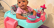 Justice is registered to the contest to win money with this photo: baby, child, cute, face, floor, happy, indoor, infant, person, pink, play, purple, seat, smiling, socks, tile, toy, turquoise, walker, young