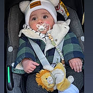 Ezio a rejoint le concours — aidez-le/la à gagner de superbes lots ! baby, car_seat, pacifier, hat, pom_poms, plush_toy, lion_toy, jacket, checkered, infant, warm_clothing, socks, child, seat_belt, cute, indoors, portrait, face, hands, cozy