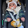 baby, car_seat, pacifier, hat, pom_poms, plush_toy, lion_toy, jacket, checkered, infant, warm_clothing, socks, child, seat_belt, cute, indoors, portrait, face, hands, cozy