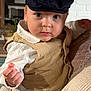 Achille participe au concours pour gagner de l'argent avec cette photo : toddler, child, cap, vest, white_shirt, indoor, person, adult_hand, knitted_sweater, face, eyes, curious, portrait, closeup, holding, furniture, home, skin, clothing, baby