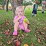 Arya is registered to the contest to win money with this photo: child, toddler, apple, grass, tree, outdoor, nature, playing, green, pink_clothing, shushing, leaves, kids, summer, sunlight, casual, sitting, footwear, people, orchard