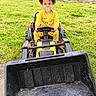 backyard, child, construction_toy, cute, daylight, excavator, fun, grass, greenery, outdoor, pacifier, person, play, sitting, steering_wheel, toddler, toy, vehicle, yellow_pajamas, young_child