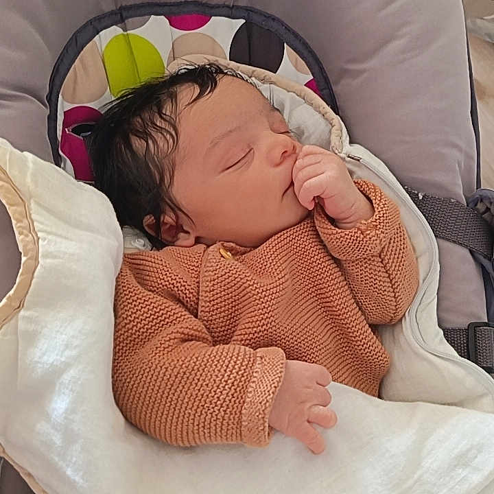 Leeroy participe au concours pour gagner de l'argent avec cette photo : baby, sleeping, infant, blanket, knitted_sweater, cushioned_seat, indoor, peaceful, child, soft, cozy, resting, curly_hair, headrest, colorful, warm_clothing, person, young_child, portrait, comfort