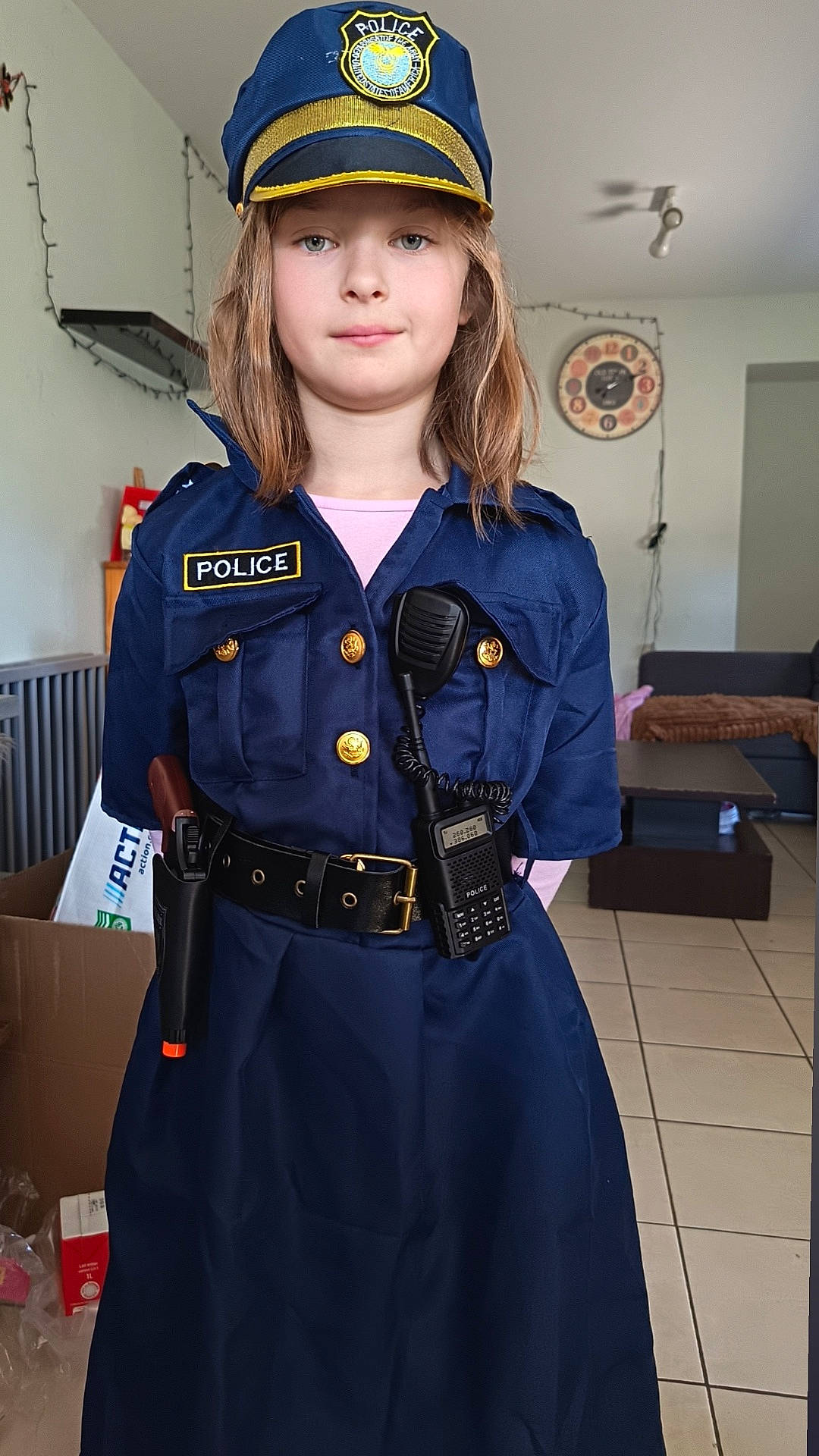 Léana a rejoint le concours — aidez-le/la à gagner de superbes lots ! blue_uniform, casual, child, clock, costume, decor, floor_tiles, furniture, hat, home, indoor, living_room, long_hair, person, police_costume, portrait, smiling, standing, toy_gun, toy_radio