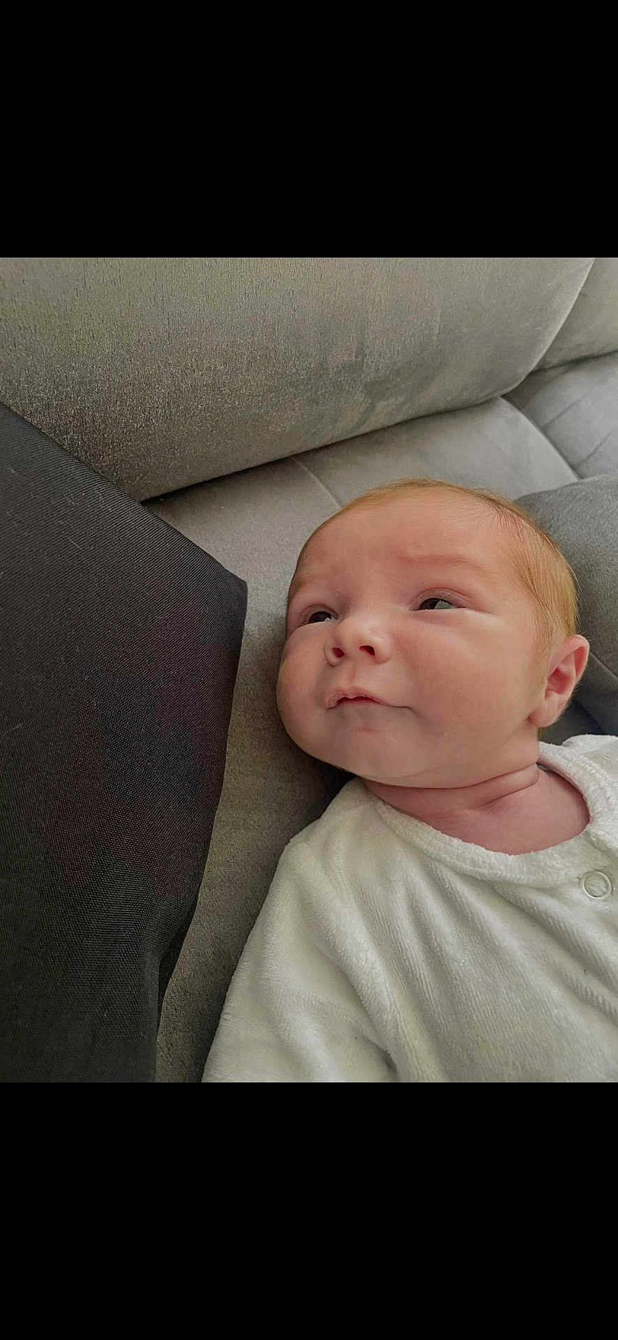 Sam a rejoint le concours — aidez-le/la à gagner de superbes lots ! baby, newborn, infant, couch, gray, white_clothing, face, head, skin, person, young_child, indoor, soft_texture, cozy, portrait, looking, resting, child, cute, expression