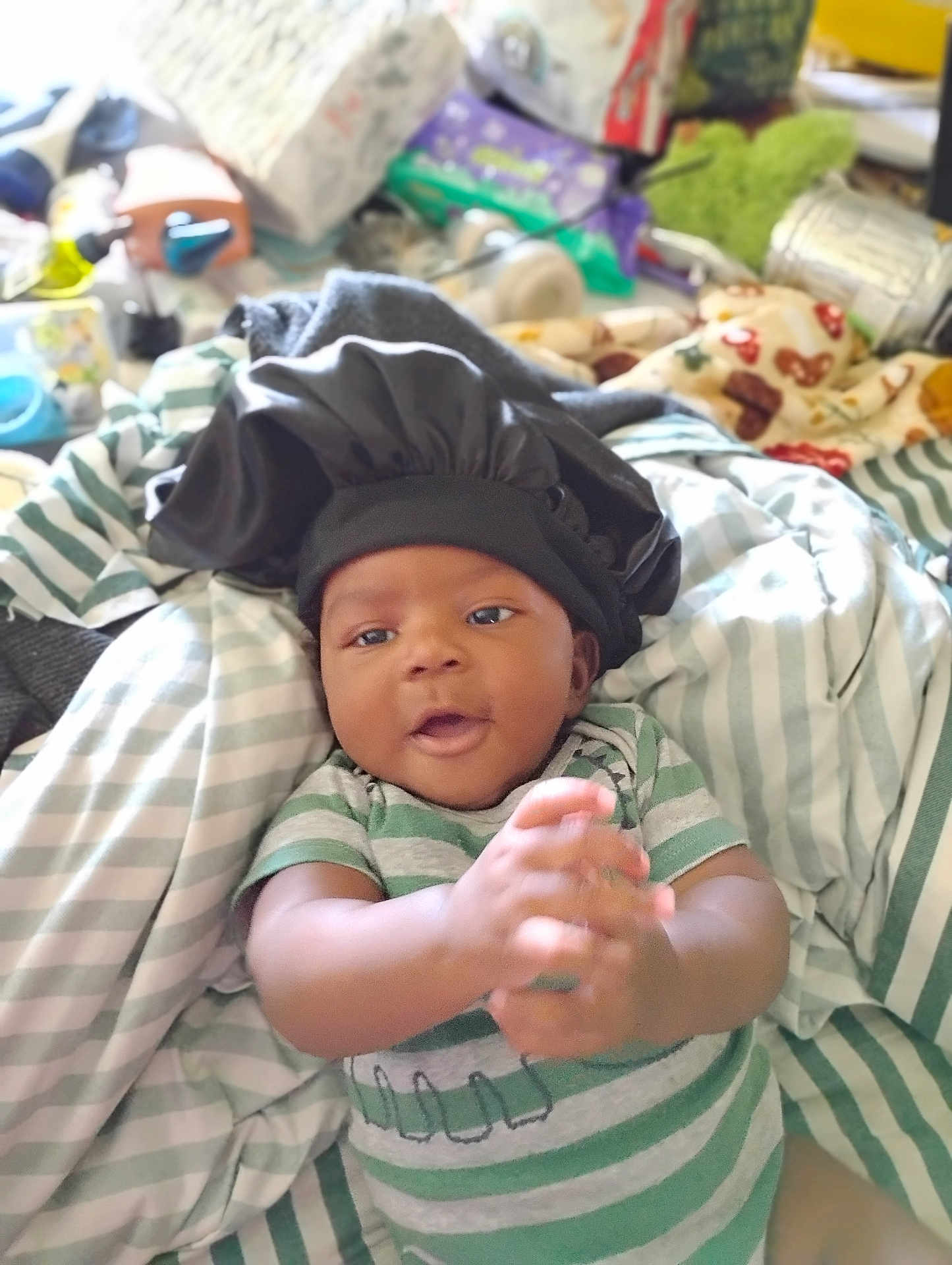 Adrian joined the competition — help win amazing prizes! baby, infant, clapping, bonnet, striped_clothing, bed, blanket, indoor, happy, cute, person, child, smiling, young, resting, fabric, soft, casual, playful, home