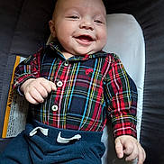 Parker is registered to the contest to win money with this photo: baby, infant, smiling, plaid_shirt, navy_pants, cushion, lying_down, happy, child, cute, portrait, indoors, clothing, buttoned_shirt, hand, face, person, young_child, casual_wear, comfort