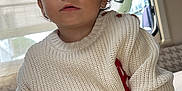 Arès a rejoint le concours — aidez-le/la à gagner de superbes lots ! toddler, child, indoors, sweater, knitwear, topknot, comb, curly_hair, face, hands, window, curtain, seated, pants, cozy, furniture, soft_lighting, expression, casual, portrait