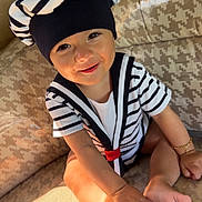 Arès a rejoint le concours — aidez-le/la à gagner de superbes lots ! baby, child, smiling, sailor_hat, striped_clothing, couch, indoor, cute, happy, face, feet, sitting, bracelet, sunlight, patterned_fabric, infant, portrait, person, cozy, playful