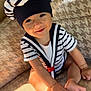 baby, child, smiling, sailor_hat, striped_clothing, couch, indoor, cute, happy, face, feet, sitting, bracelet, sunlight, patterned_fabric, infant, portrait, person, cozy, playful