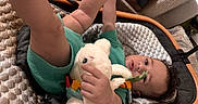 Rhythm joined the competition — help win amazing prizes! baby, infant, stuffed_animal, toy, cushion, seat, green_clothing, hand, foot, face, curious, indoor, child, soft_toy, playful, legs, expression, person, blanket, relaxing
