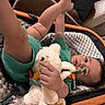 baby, infant, stuffed_animal, toy, cushion, seat, green_clothing, hand, foot, face, curious, indoor, child, soft_toy, playful, legs, expression, person, blanket, relaxing