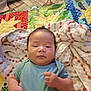 baby, infant, quilt, blanket, towel, blue_shirt, indoor, child, face, head, fist, lying_down, colorful, patterned, soft_texture, young_child, skin, person, portrait, cute