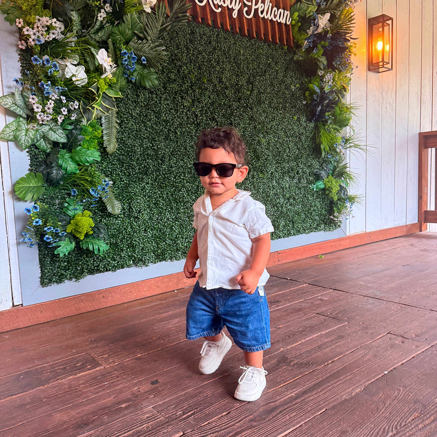 George joined the competition — help win amazing prizes! child, toddler, boy, portrait, sunglasses, white_shirt, denim_shorts, sneakers, standing, walking, outdoor, restaurant, floral_wall, greenery, flowers, wooden_deck, sign, decor, fashion, confident