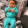baby, child, infant, smiling, blue_clothing, hoodie, pants, socks, pillow, blanket, indoor, cute, portrait, person, young_child, furniture, pattern, resting, happy, cozy