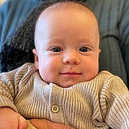 Ezra a rejoint le concours — aidez-le/la à gagner de superbes lots ! baby, infant, face, eyes, smile, hand, knitted_sweater, beige, cozy, close_up, skin, person, cute, child, portrait, warm, soft, indoor, holding, young