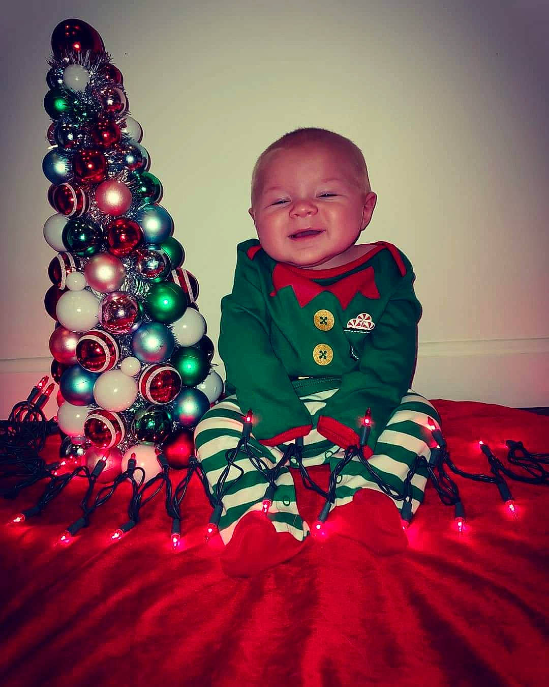 Kaedyn joined the competition — help win amazing prizes! child, christmas, christmas_decoration, christmas_eve, christmas_lights, christmas_ornament, christmas_tree, event, fun, holiday, holiday_ornament, interior_design, lighting, outerwear, person, red, sitting, standing, toddler, tradition