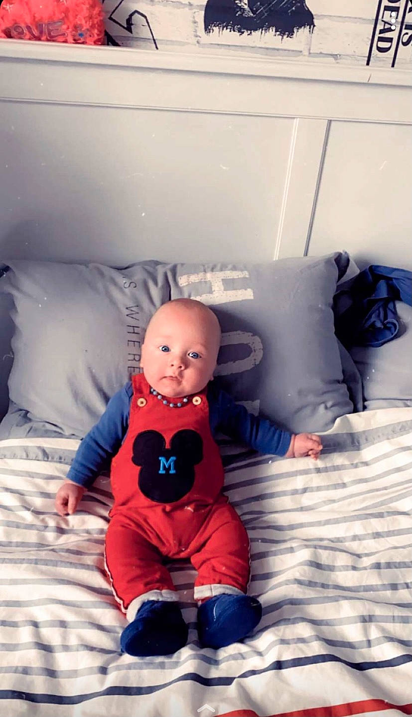 Aaron a rejoint le concours — aidez-le/la à gagner de superbes lots ! baby, baby_toddler_clothing, bed, bed_sheet, bedding, bedroom, blanket, comfort, human_body, linens, overall, person, pillow, room, sitting, throw_pillow, toddler