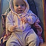 baby, child, hoodie, blanket, cushion, chair, indoor, smiling, tongue_out, sitting, cute, infant, warm_clothing, person, soft_lighting, cozy, plush, face, portrait, happy