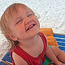 child, toddler, beach, seaside, sand, ocean, water, lounge_chair, smiling, laughing, portrait, outdoor, vacation, summer, red_shirt, green_shorts, blonde_hair, sunny, family, happy