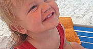 Janco is registered to the contest to win money with this photo: child, toddler, smiling, beach, sandy_beach, seaside, ocean, sunny, outdoor, portrait, red_shirt, green_shorts, lounge_chair, orange_towel, vacation, summer, blonde_hair, blue_water, sunbathers, happy