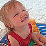child, toddler, smiling, beach, sandy_beach, seaside, ocean, sunny, outdoor, portrait, red_shirt, green_shorts, lounge_chair, orange_towel, vacation, summer, blonde_hair, blue_water, sunbathers, happy