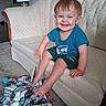toddler, child, smiling, happy, portrait, sitting, couch, sofa, blanket, toy, living_room, lamp, carpet, indoor, home, blue_shirt, green_shorts, red_hair, playful, photograph