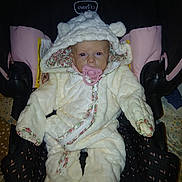 Winter is registered to the contest to win money with this photo: baby, child, pacifier, snowsuit, white, fluffy, car_seat, pink, hood, ears, floral_trim, infant, cute, warm_clothing, seated, indoor, portrait, looking_at_camera, serious_expression, soft_texture