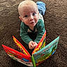 baby, child, reading, book, carpet, floor, indoor, curious, green_shirt, blue_jeans, expression, young, person, play, colorful, illustration, frogs, storybook, lying_down, close_up
