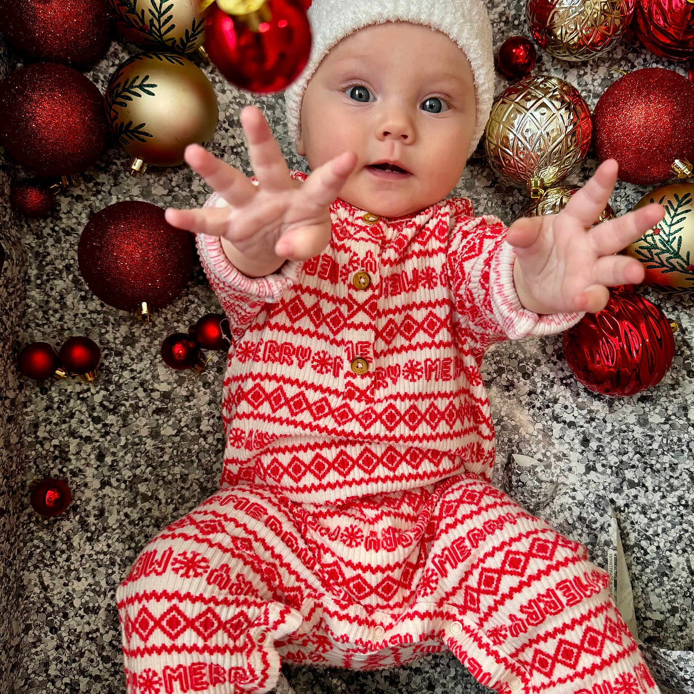 Elizabeth Kopylova is registered to the contest to win money with this photo: baby, celebration, child, christmas, cute, decorations, eyes, face, festive, floor, hands, holiday, infant, ornaments, pajamas, patterned, reaching, red, santa_hat, white
