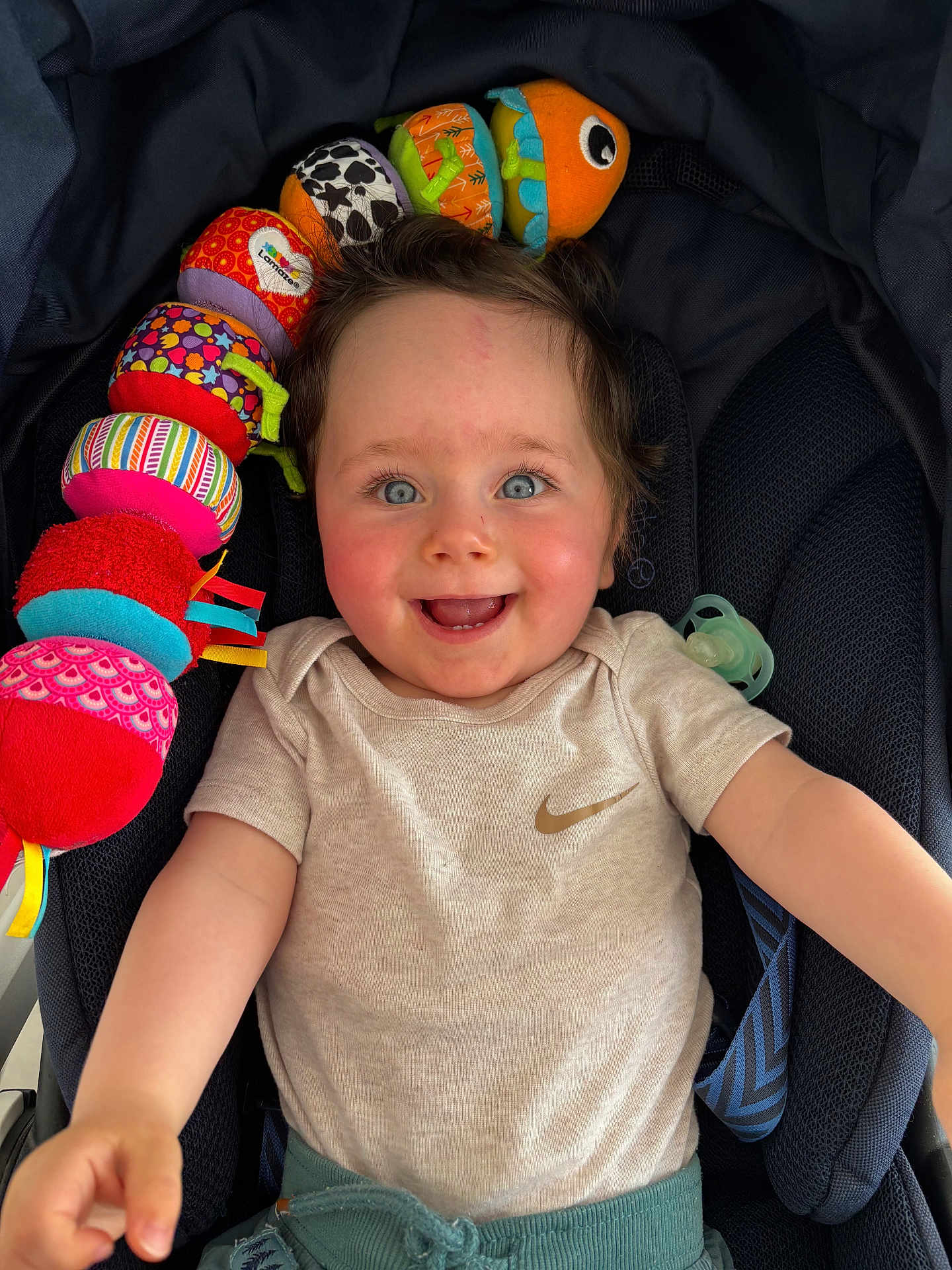 Romain a rejoint le concours — aidez-le/la à gagner de superbes lots ! baby, smiling, blue_eyes, plush_toy, caterpillar_toy, stroller, clothing, beige_shirt, teal_pants, happy, child, cute, infant, person, indoor, portrait, playful, reaching_out, seat, pacifier