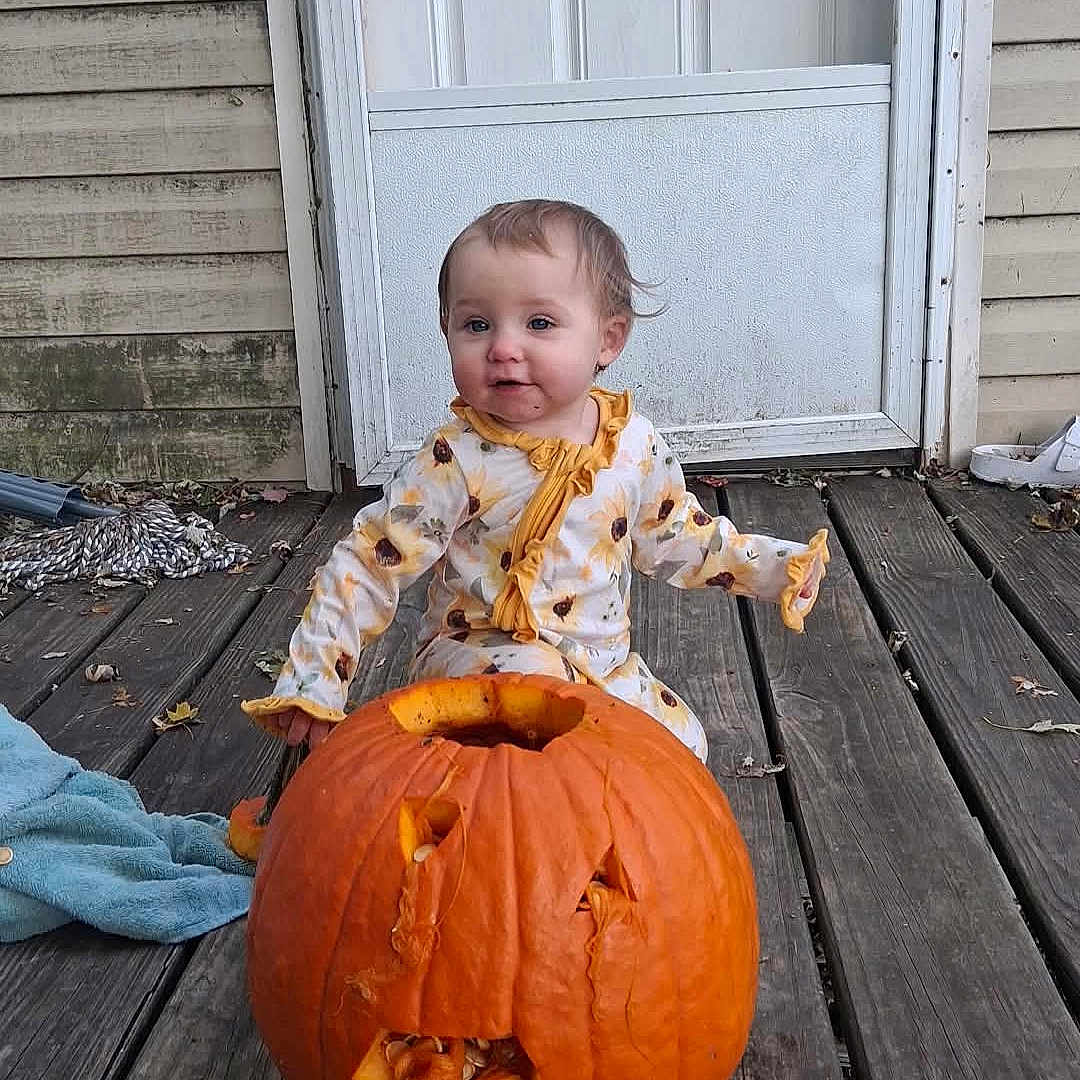 Blakeleigh Fisher is registered to the contest to win money with this photo: autumn, baby, child, curly_hair, door, door_handle, face, fall, holiday, jack_o_lantern, outdoor, pajamas, person, pumpkin, seasonal, smiling, sunflower_pattern, toddler, wood, wooden_porch