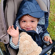 Noa a rejoint le concours — aidez-le/la à gagner de superbes lots ! toddler, child, stroller, teddy_bear, hooded_jacket, smiling, waving, outdoor, grass, toy, baby, person, cute, happy, seat, clothing, hand, face, portrait, baby_carriage